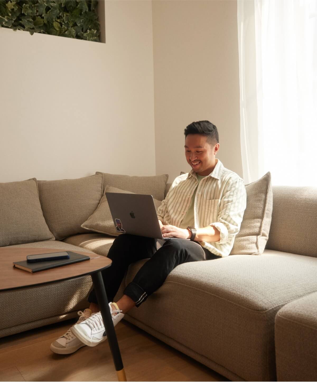 Heureux de travailler à domicile : une personne souriante travaillant sur son divan, mettant en valeur la productivité et le confort dans un environnement de travail à distance